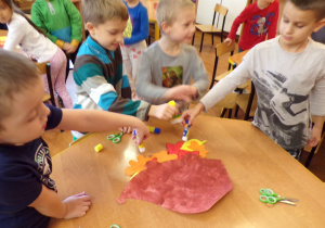 Dzieci przyklejajace papierowego jeza do liści.